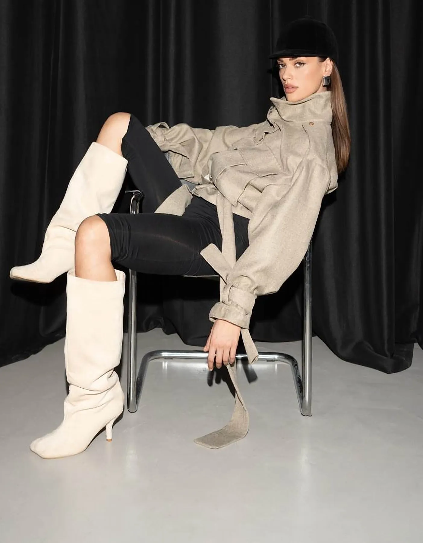 Model seated in a beige utility jacket and cream knee boots