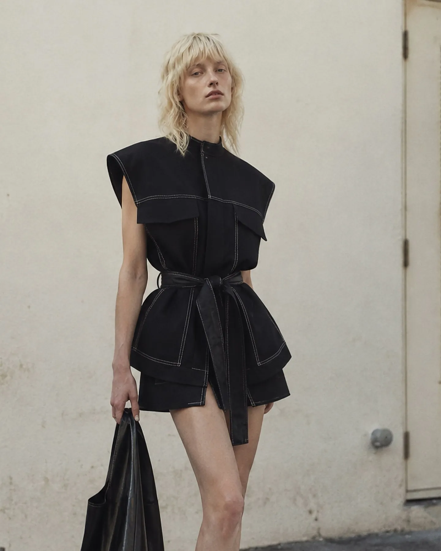 Model in a black structured vest with contrast stitching and shorts, full look